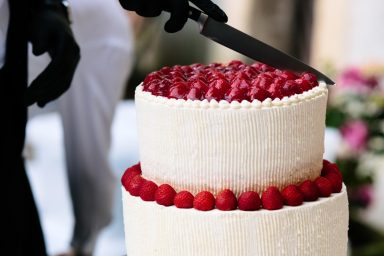 Torte Eine Hochzeitstorte mit roten Beeren wird mit einem Messer angeschnitten.