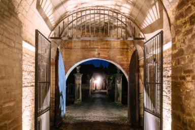 Event 5 Blick durch einen beleuchteten Torbogen auf einen gepflasterten Weg in der Dämmerung.