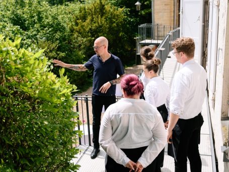 Eine Gruppe von Menschen hört einem Mann mit Brille zu, der auf Pflanzen zeigt.