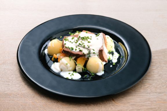 Ein Teller mit gekochtem Fisch, Kartoffeln und Sahnesauce, garniert mit Schnittlauch.