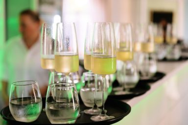 Sektempfang 2 Eine Reihe von Gläsern mit Getränken auf einem Tablett, im Hintergrund eine unscharfe Person.