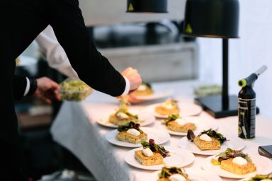 Anrichten 2 Ein Koch richtet mehrere kleine Teller mit Speisen unter warmen Lampen an.