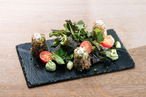 Ein kunstvoll angerichteter Teller mit Salat, Tomaten und Kräutercreme.