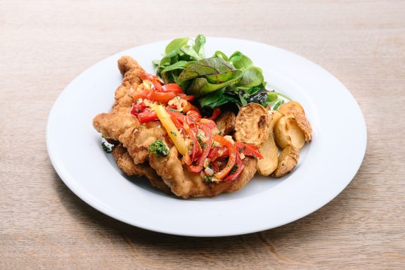Frittierte Hähnchenbrust mit Paprika und frischem Salat auf einem weißen Teller.