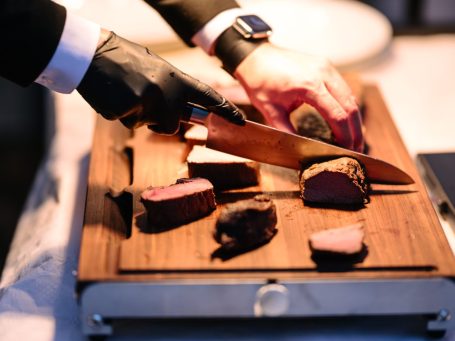 Ein Koch schneidet Fleisch auf einem Holzbrett mit einem großen Messer.