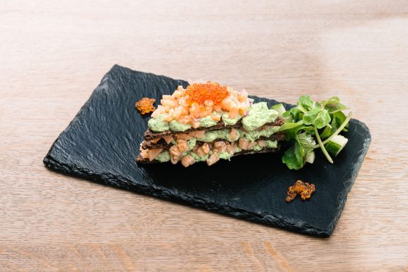 Schwarzer Steinplatte mit geschichteten Sushi-Zutaten, garniert mit Meerrettich und Rucola.