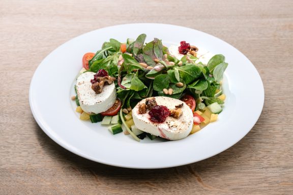 Frisch zubereiteter Salat mit Käse, Gemüse und frischen Kräutern auf einem weißen Teller.