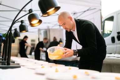 Anrichten 4 Ein Koch arrangiert Lebensmittel unter Markisen mit beleuchteten Tischen.