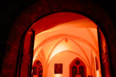 Event Blick durch einen roten, beleuchteten Bogen in einen historischen Raum mit gotischen Elementen.