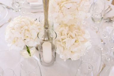 Deko Ein Tischgedeck mit weißen Blumen und einem Glas mit einer Kerze.