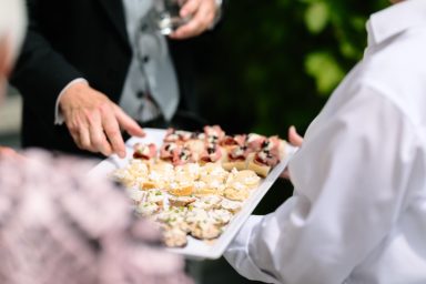 Service Hände reichen ein Tablett mit verschiedenen Snacks auf einer eleganten Veranstaltung.