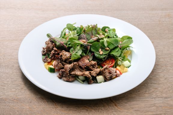 Ein Teller mit Fleisch, frischem Gemüse und grünen Blättern, dekoriert mit Nüssen.