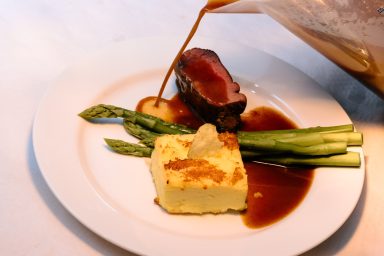 Anrichten Rinderfilet mit Sauce, Spargel und einer Portion pürierter Beilage auf einem Teller.