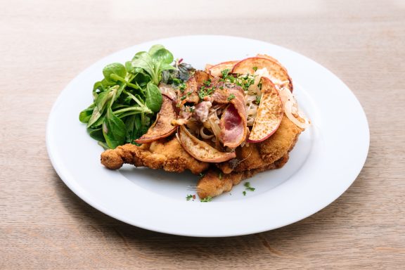 Frittierte Hähnchenkeule mit Äpfeln und frischem Salat auf einem weißen Teller.